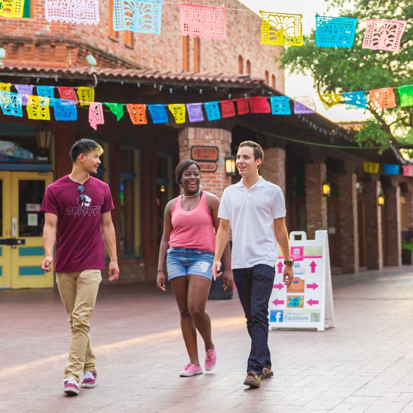 three ԰ students walk through Market Square under papel picado